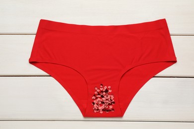 Photo of Woman's panties with red sequins on white wooden background, top view. Menstrual cycle