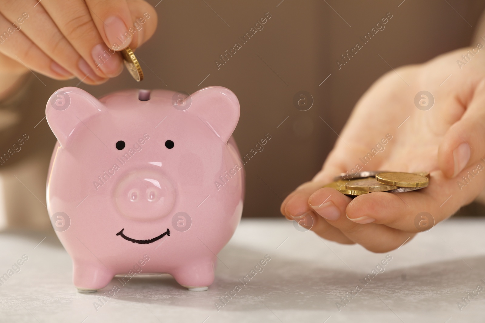 Photo of Pension savings. Woman putting coins into piggy bank at light grey table, closeup