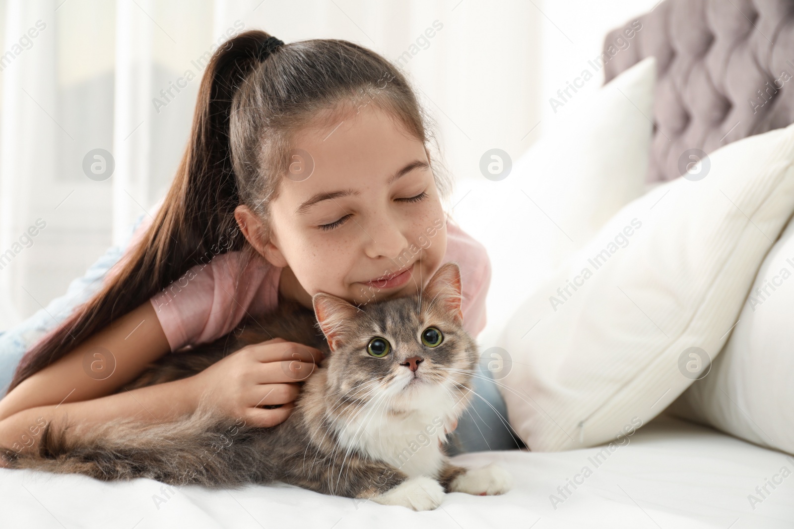 Photo of Cute little girl with cat lying on bed at home. First pet