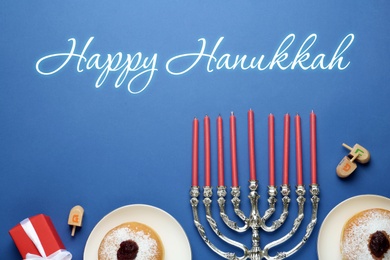 Image of Happy Hanukkah. Traditional menorah, candles, sufganiyot and dreidels on blue background, flat lay 