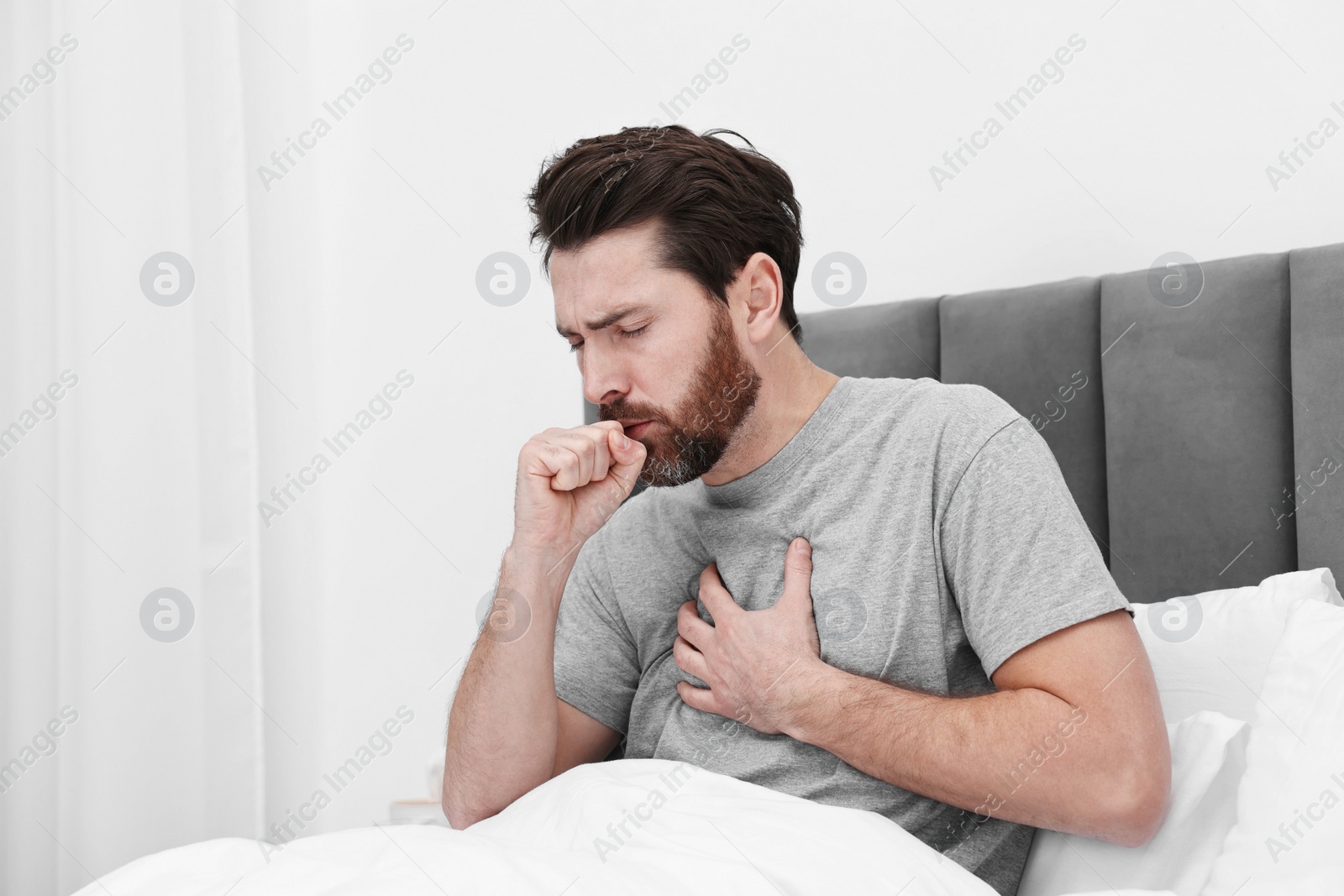 Photo of Sick man coughing on bed at home. Cold symptoms