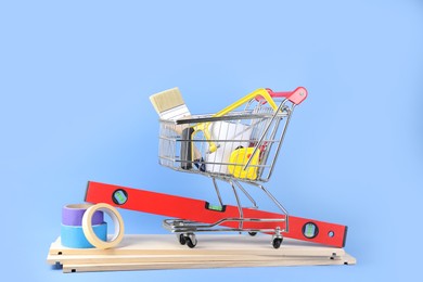 Small shopping cart with paint and renovation equipment on light blue background