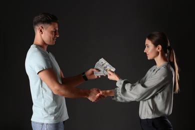 Photo of Woman shaking hands with man and offering bribe on black background