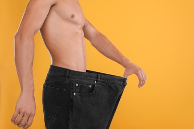 Photo of Shirtless man with slim body wearing big jeans on yellow background, closeup