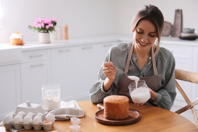 Photo of Young woman decorating traditional Easter cake with glaze in kitchen. Space for text