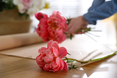 Photo of Florist making beautiful bouquet at table, focus on peony