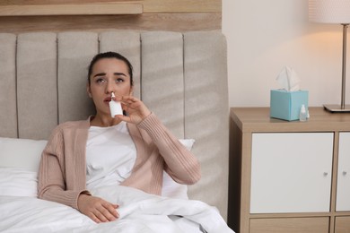 Photo of Sick young woman using nasal spray in bed at home