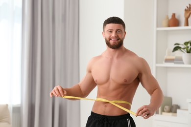 Photo of Happy athletic man measuring waist with tape at home, space for text. Weight loss concept