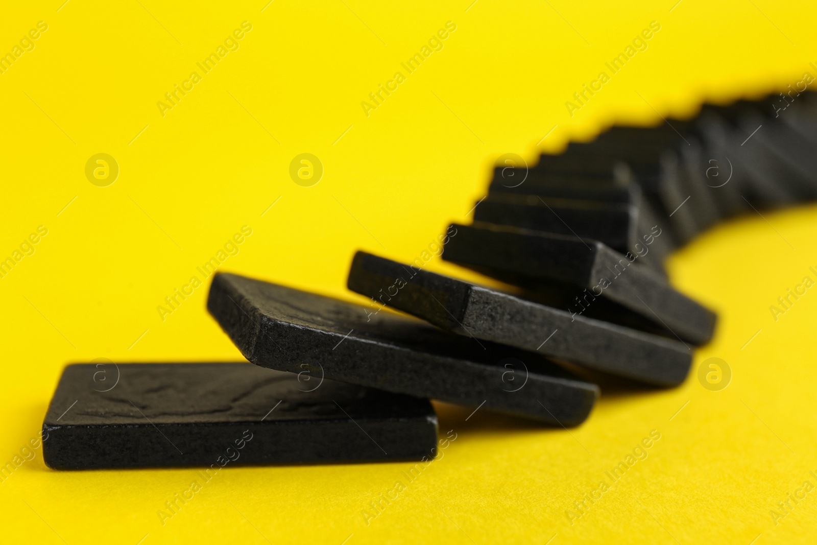 Photo of Falling black domino tiles on yellow background, closeup