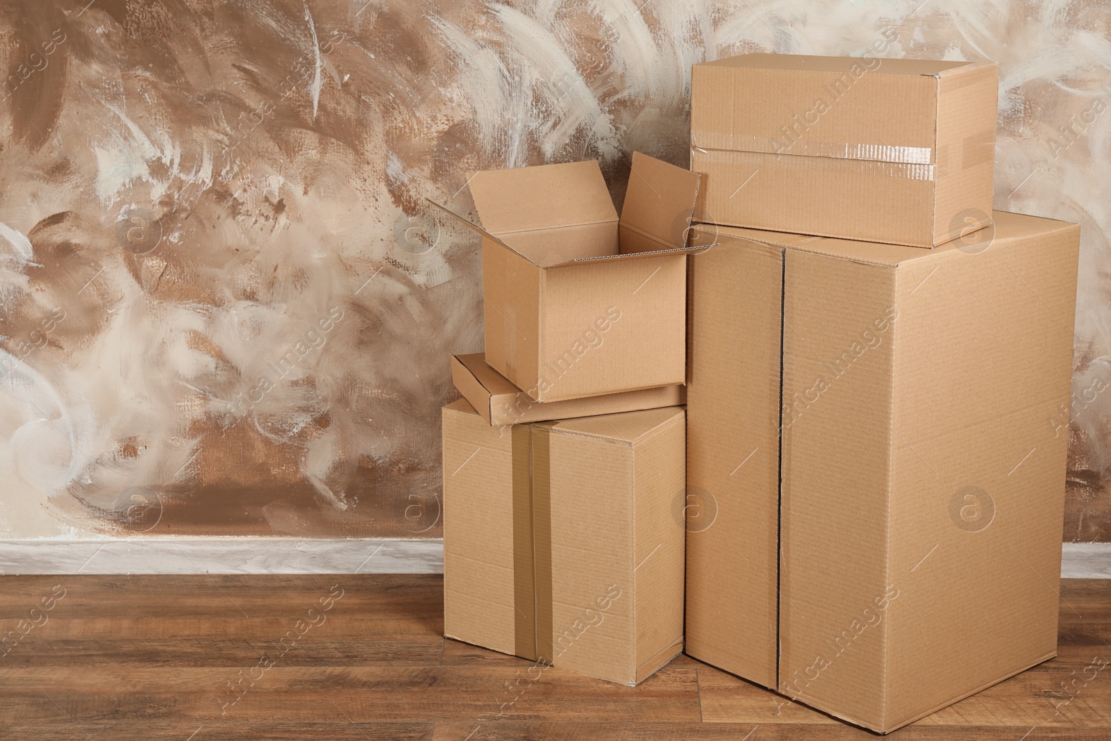 Photo of Pile of cardboard boxes near brown wall indoors. Space for text