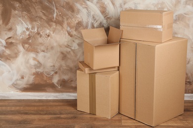 Photo of Pile of cardboard boxes near brown wall indoors. Space for text