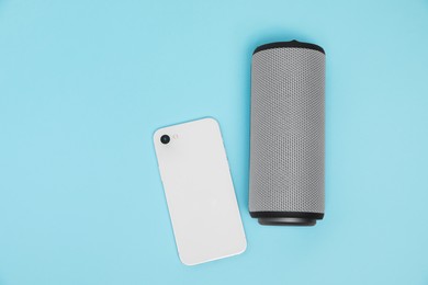 Photo of Portable bluetooth speaker and smartphone on light blue background, flat lay with space for text. Audio equipment