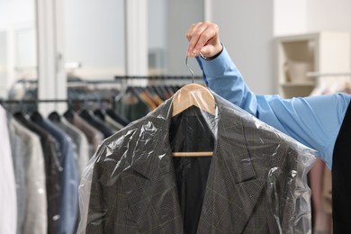 Photo of Dry-cleaning service. Woman holding jacket in plastic bag indoors, closeup