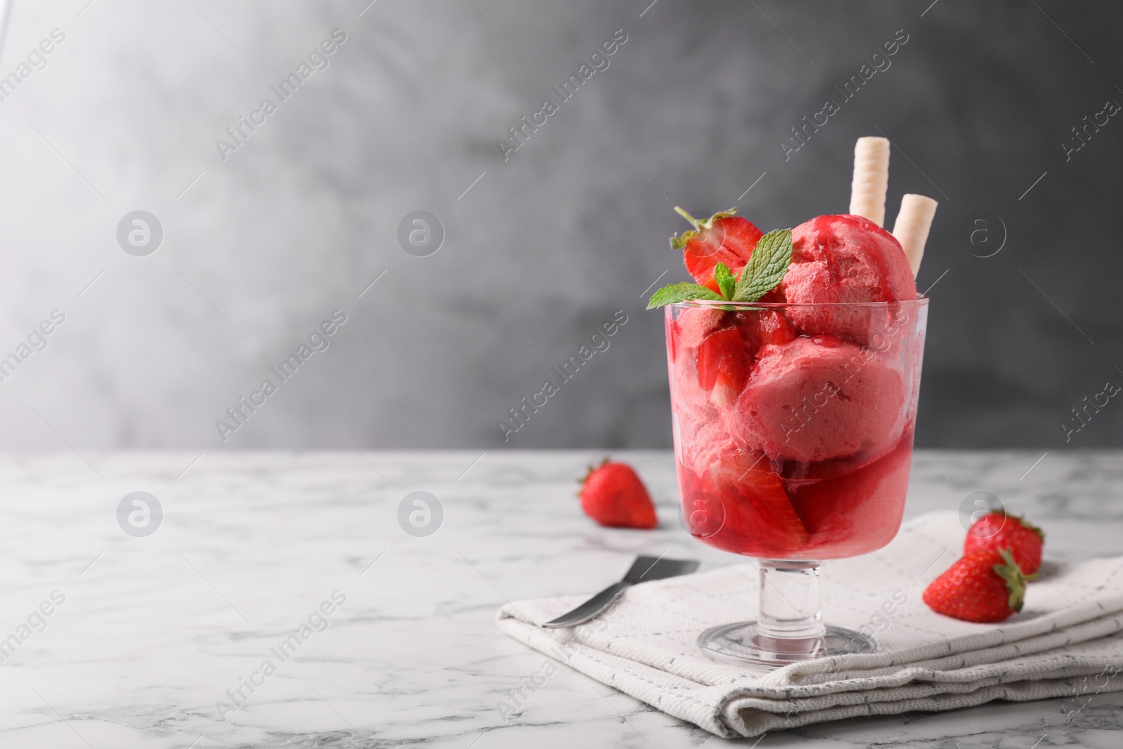 Photo of Tasty strawberry ice cream with fresh berries and wafer rolls in glass dessert bowl on white marble table. Space for text