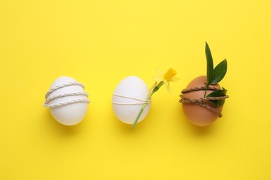 Easter eggs decorated with green leaves and flower on yellow background, flat lay