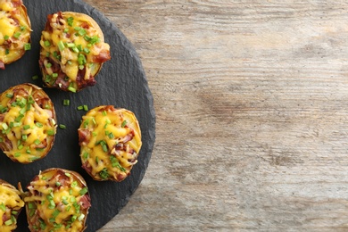 Slate plate with baked potatoes on wooden background, top view with space for text