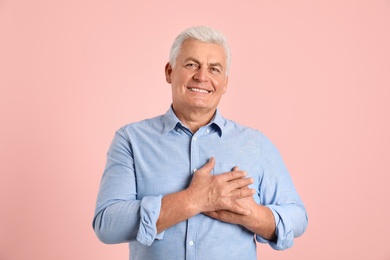 Photo of Portrait of mature holding hands on his heart against color background