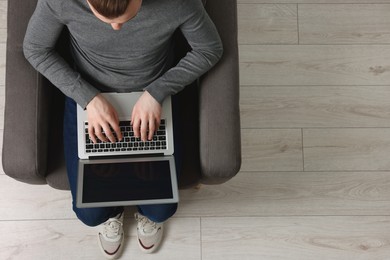 Photo of Man working with laptop in armchair, top view. Space for text