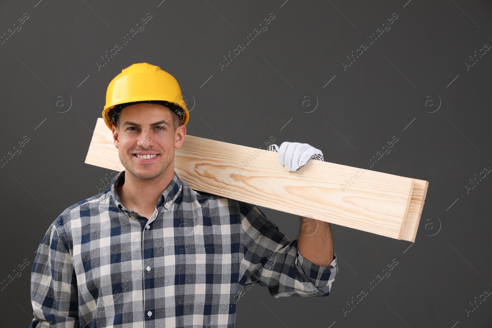 Photo of Handsome carpenter with wooden planks on dark background