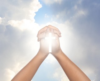 Image of Religion. Christian woman with glowing cross praying against sky, closeup