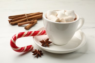 Photo of Tasty hot chocolate with marshmallows, candy cane and spices on white marble table, closeup