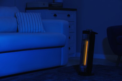 Photo of Electric infrared heater in dark living room at night
