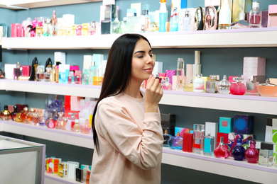 Image of Beautiful young woman choosing perfume in shop