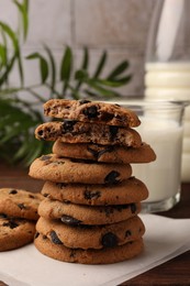 Photo of Stack of delicious chocolate chip cookies and milk on wooden table
