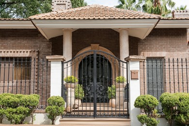 Black metal gates near beautiful house and plants outdoors