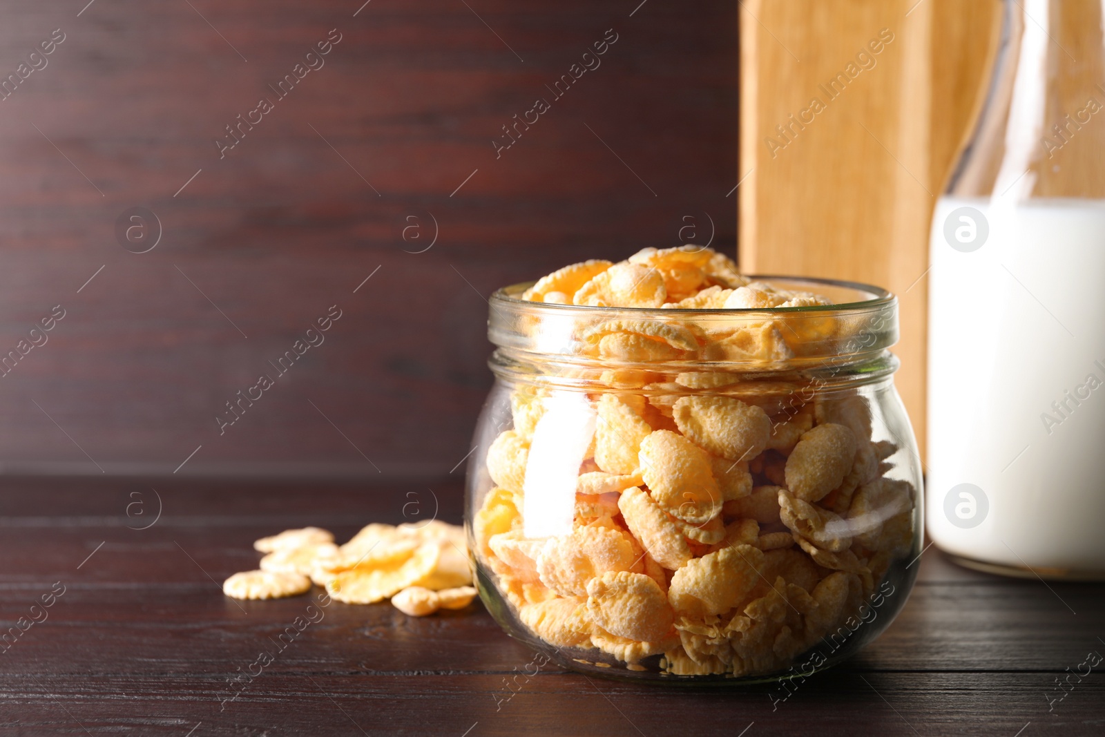 Photo of Jar of tasty crispy corn flakes on wooden table, space for text