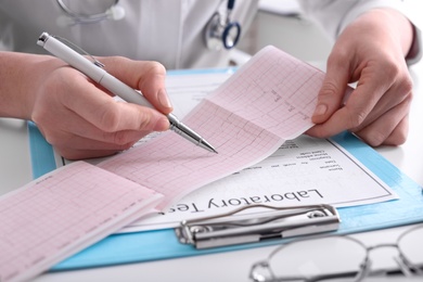 Photo of Doctor examining cardiogram at table in clinic, closeup