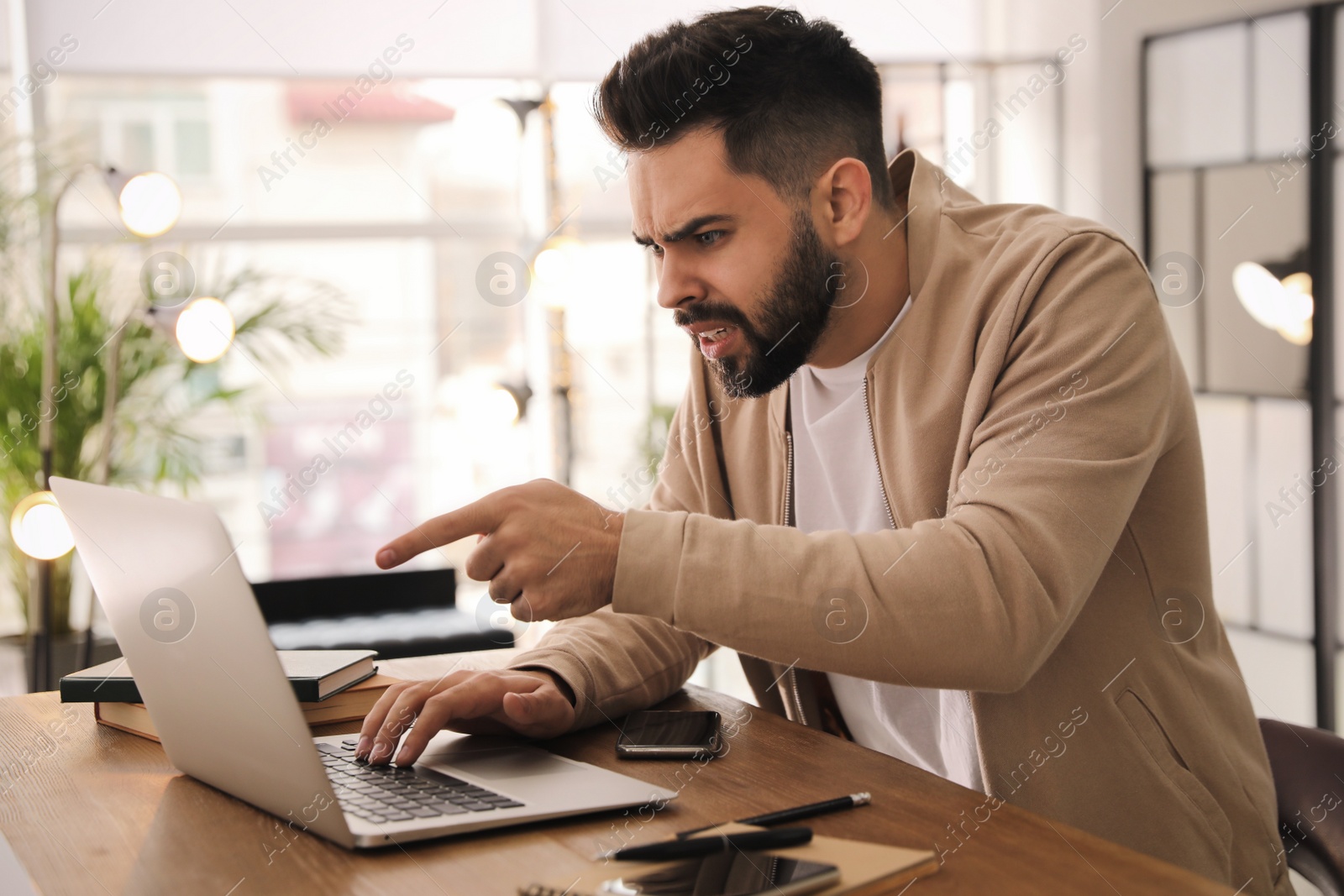 Photo of Emotional young man working on laptop in office. Online hate concept