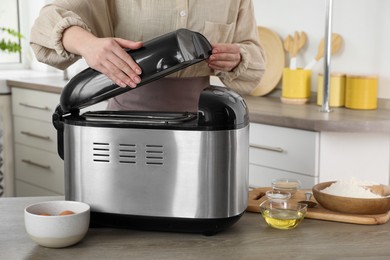 Woman using breadmaker machine at wooden table in kitchen, closeup