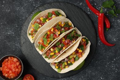 Tasty tacos with vegetables on black textured table, flat lay