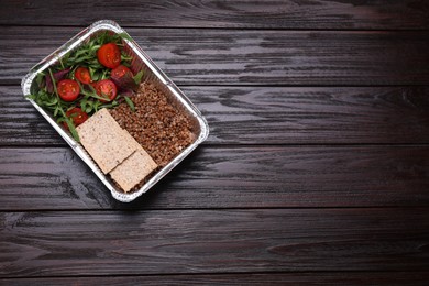 Container with buckwheat, fresh salad and crispbreads on wooden table, top view. Space for text