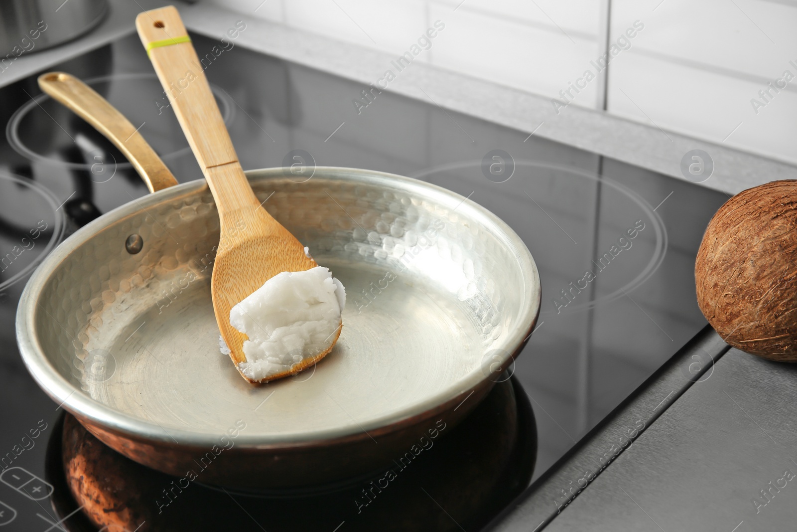 Photo of Wooden spatula with coconut oil in frying pan. Healthy cooking