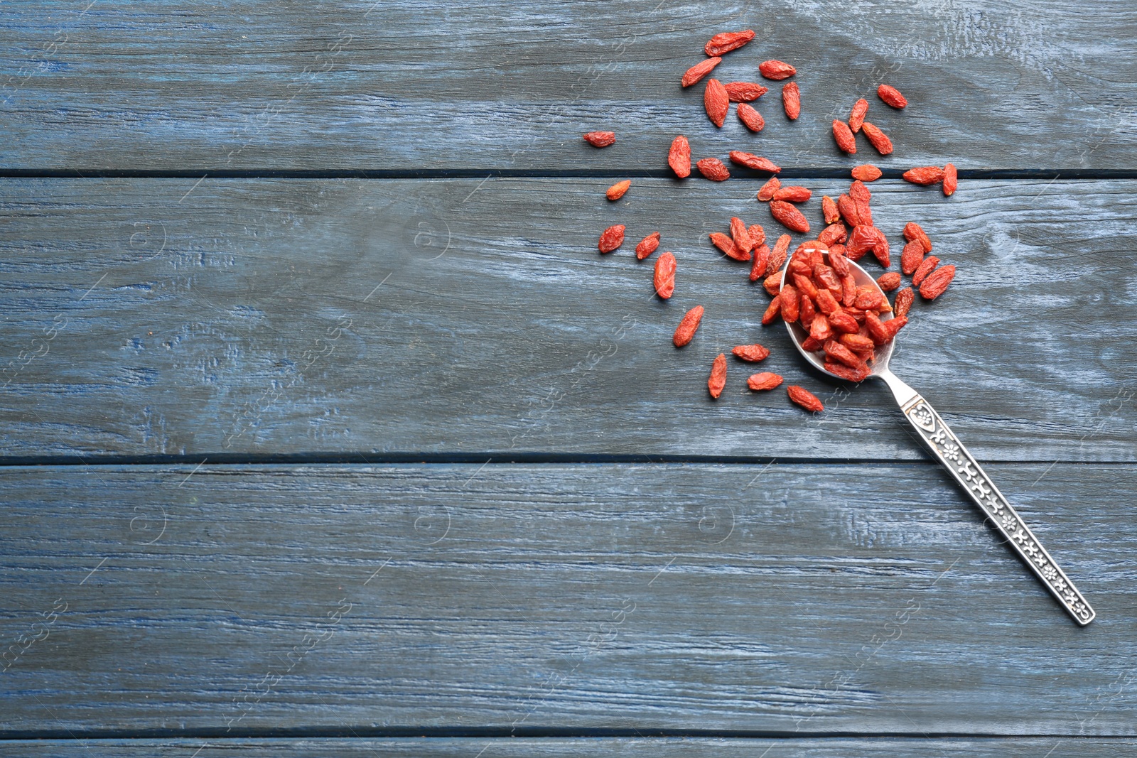 Photo of Spoon and dried goji berries on blue wooden table, top view with space for text. Healthy superfood