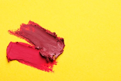 Smears of bright lipsticks on yellow background, top view. Space for text