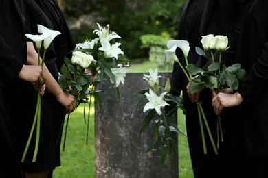 Photo of People with flowers near granite tombstone at cemetery outdoors, closeup. Funeral ceremony