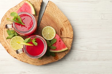 Photo of Glass mason jars with tasty summer watermelon drink, limes and mint on white wooden table, top view. Space for text
