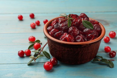 Photo of Tasty dried cranberries in bowl, fresh ones and leaves on light blue wooden table, closeup