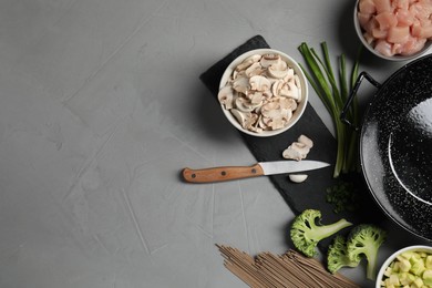 Photo of Wok pan, noodles, chicken and other products on light grey table, flat lay. Space for text