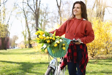 Beautiful woman with bicycle and bouquet of yellow tulips in park