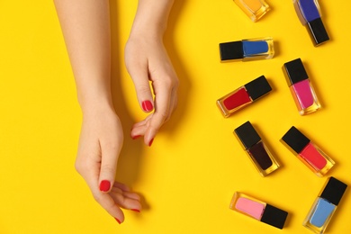 Woman with red manicure and nail polish bottles on color background, top view