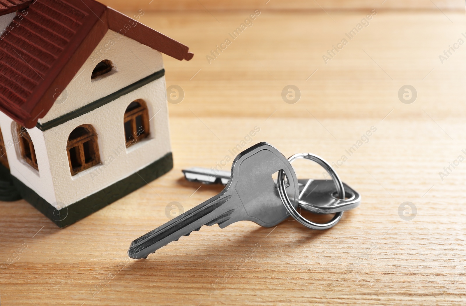 Photo of Keys and house model on wooden table. Real estate agent services