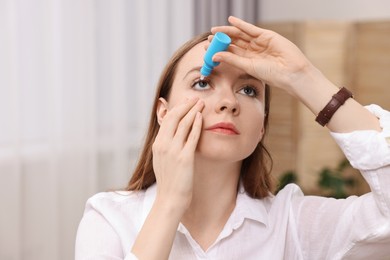 Young woman applying medical eye drops indoors