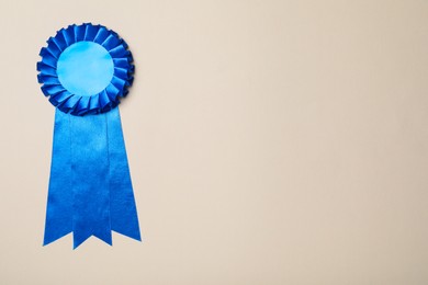 Photo of Blue award ribbon on beige background, top view. Space for text