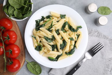 Photo of Tasty pasta with spinach and sauce served on grey textured table, flat lay