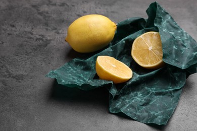 Photo of Whole and cut fresh lemons with beeswax food wrap on grey table
