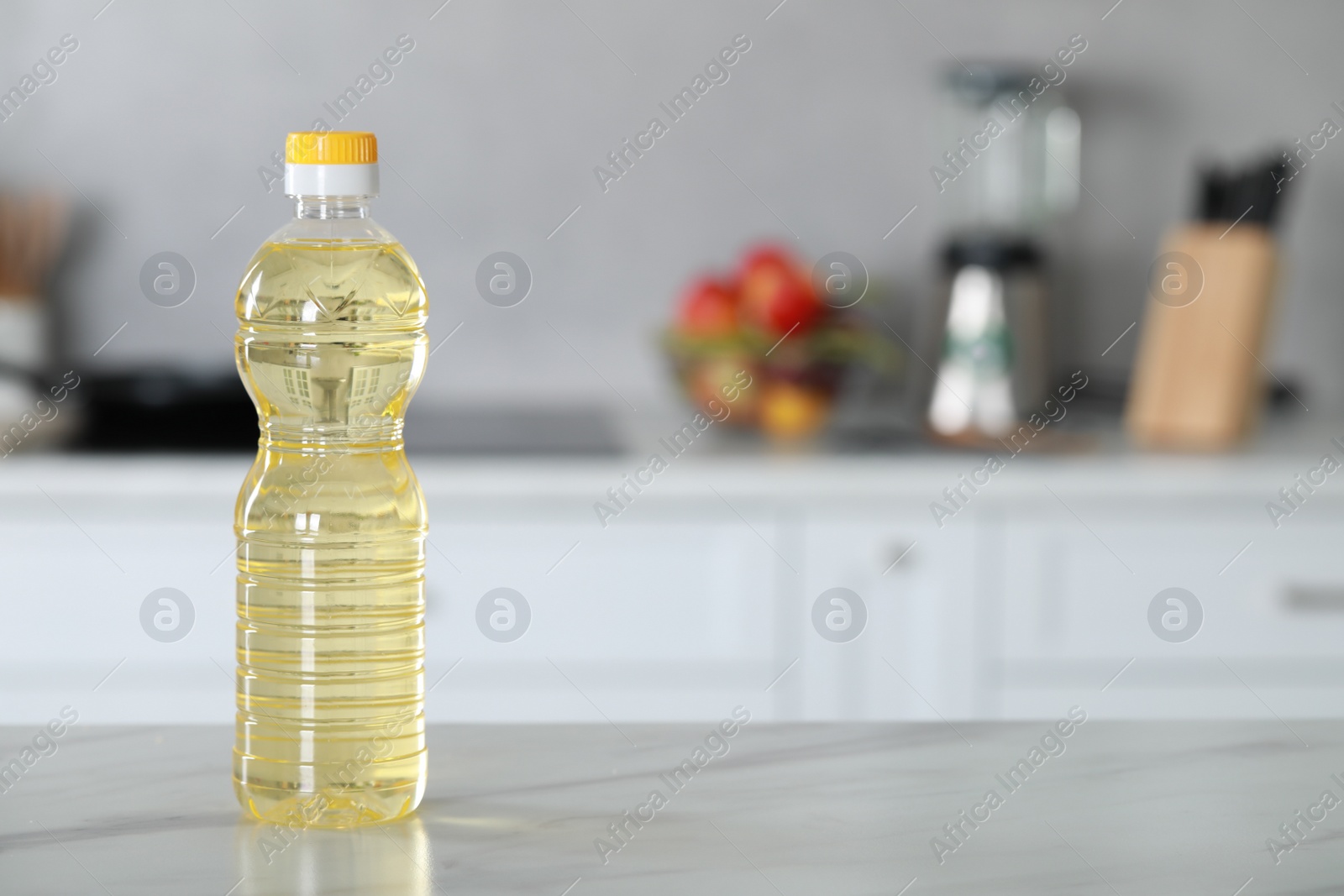 Photo of Bottle of cooking oil on white marble table in kitchen. Space for text